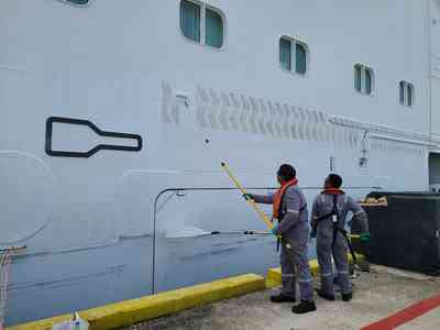 Crew painting over the 'mule' tractor marks left on the hull from the canal transit.